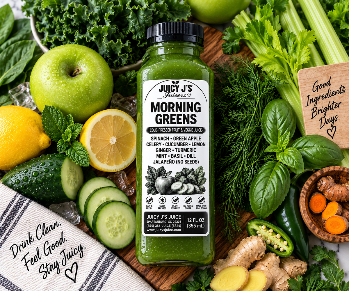 Juicy J's Organic Morning Greens smoothie blend in a clear plastic bottle with a black cap, surrounded by fresh green ingredients like celery, kale, spinach, cucumber, lemon, basil, ginger, and turmeric on a wooden board.